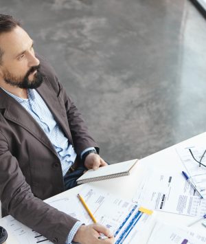 Thoughtful middle aged businessman generates new ideas on developmant of company, tries to find successful solution and climb career ladder, works with many official documents, has clever expression